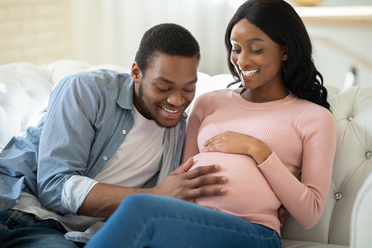 Positive black man touching his pregnant girlfriend's tummy, communicating with baby, feeling its movements at home